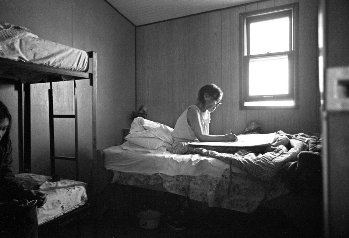 Art Canada Institute, Pitseolak drawing in bed in her son Kumwartok’s house, c. 1975