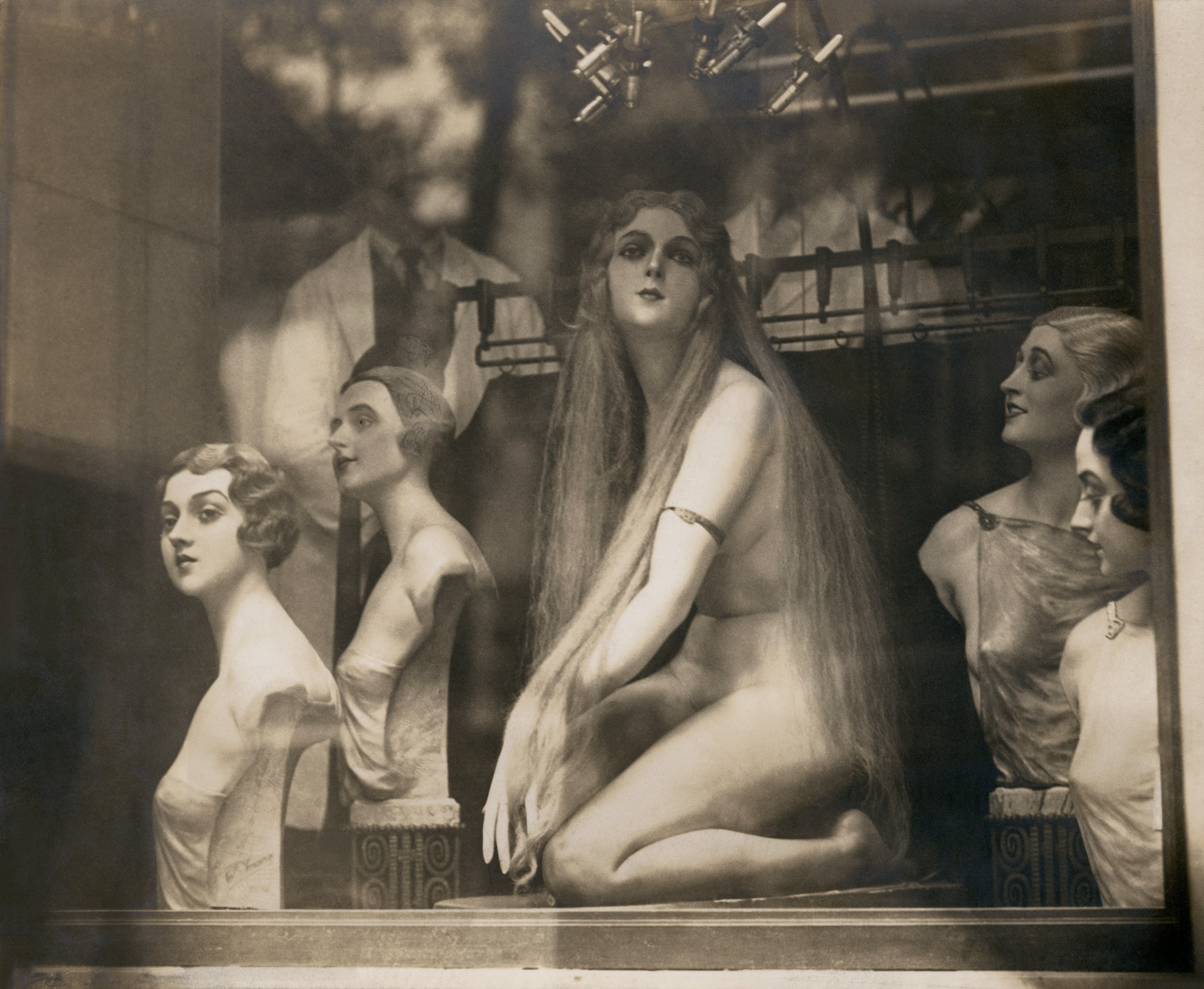 A black and white photo of a storefront with several mannequins in various poses